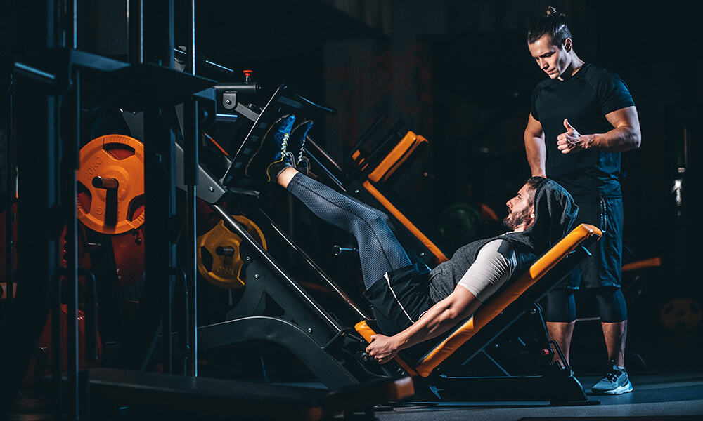 a coach cuing his client while performing leg press